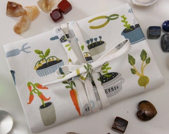 May include: A white fabric pouch with a green, blue, and orange pattern of plants and gardening tools. The pouch is tied with a white ribbon and the text "ERBSE" is visible on the pouch.