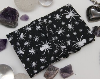 May include: A black fabric journal with a white spider pattern. The journal is closed and tied with a black ribbon. The journal is surrounded by various crystals and other decorative items.