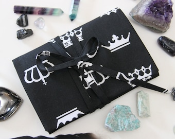 May include: A black fabric pouch with a white crown pattern, tied with a black ribbon. The pouch is surrounded by various crystals and stones, including amethyst, fluorite, and green aventurine.