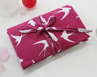 May include: A pink fabric pouch with a white swallow pattern is tied with a pink ribbon. The pouch is on a white surface with pink and clear glass stones.
