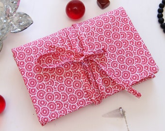 May include: A red and white fabric pouch with a circular pattern, tied with a red ribbon. The pouch is folded and sitting on a white surface.