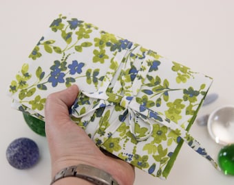May include: A white fabric journal with a green and blue floral pattern. The journal is tied closed with a white ribbon.