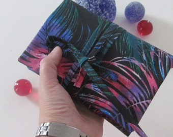 May include: A black clutch with a tropical leaf pattern in shades of blue, pink, and green. The clutch is tied with a matching fabric tie. Decorative glass spheres in blue and red are in the background.