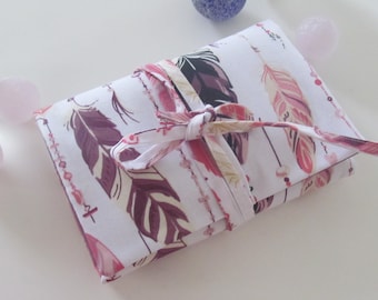 May include: A white fabric pouch with a pink and purple feather pattern. The pouch is tied with a pink ribbon and has a white background.