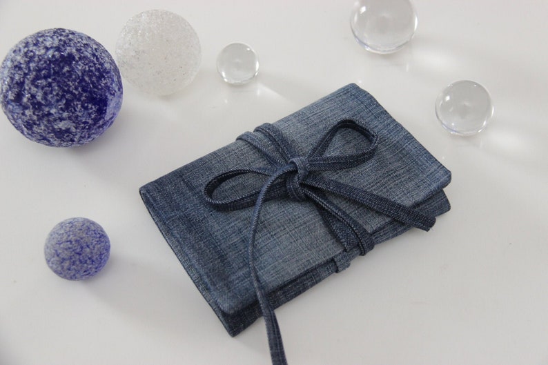 Puede incluir: Una peque&ntilde;a bolsa de mezclilla azul atada con una cinta azul. La bolsa est&aacute; sobre una superficie blanca con varias esferas de vidrio.