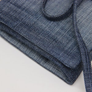 Puede incluir: Una bolsa de lona azul con una larga correa de lona azul. La bolsa est&aacute; doblada y la correa est&aacute; atada en un nudo.