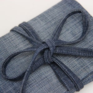 Puede incluir: Una bolsa de lona azul con cierre de corbata de lona azul. La bolsa est&aacute; doblada y atada con la corbata.