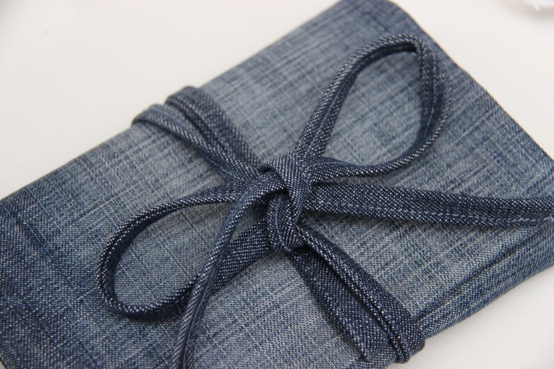 Puede incluir: Una bolsa de lona azul con cierre de corbata de lona azul. La bolsa est&aacute; doblada y atada con la corbata.