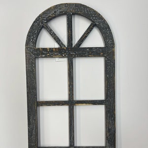 May include: A black wooden window frame with a distressed finish. The frame has a half-circle arch at the top and a grid of four panes.
