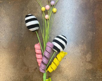 May include: A black and white striped Easter egg with yellow, pink and purple curly ribbon accents and a green stem with small yellow, pink and purple balls.