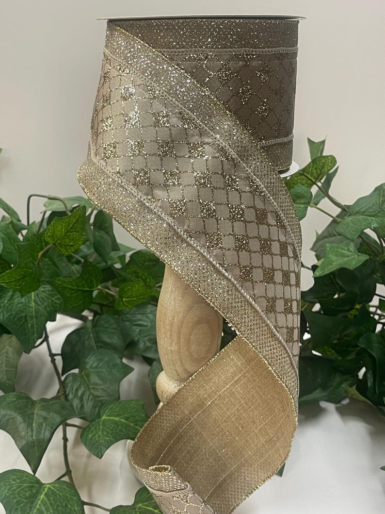 Peut inclure: Un rouleau de ruban d&eacute;coratif marron et dor&eacute;. Le ruban pr&eacute;sente un motif quadrill&eacute; avec des accents de paillettes et une bordure dor&eacute;e. Le ruban est pr&eacute;sent&eacute; sur une bobine en bois, avec un feuillage vert en arri&egrave;re-plan.
