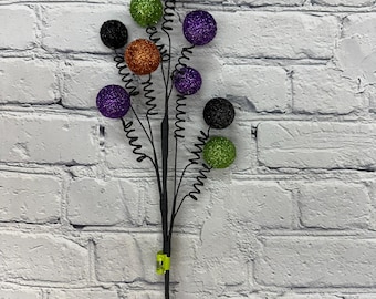May include: A black wire stem with multiple branches, each topped with a glittery ball. The balls are in various colors, including black, green, orange, and purple.