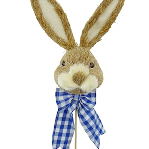 May include: A brown bunny head with a blue and white gingham bow, attached to a wooden stick. The bunny head is made of straw-like material.