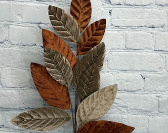 May include: A decorative artificial branch featuring multiple oval-shaped leaves with a textured, velvet-like finish. The leaves alternate in colour between deep burnt orange and muted taupe, each displaying a prominent central vein and side veins.