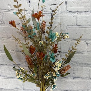 May include: A bouquet of artificial flowers with teal, orange, and white accents. The bouquet features a variety of textures and colors, including small berries, leaves, and flowers.