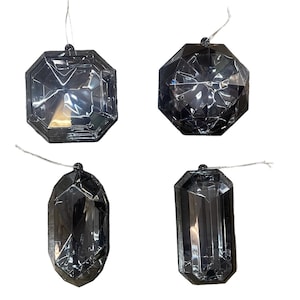 May include: Four faceted, black, jewel-shaped ornaments with silver string hangers. The ornaments have different geometric shapes, including octagons, spheres, and elongated rectangles. These decorative ornaments are suitable for holiday or special occasion decor.