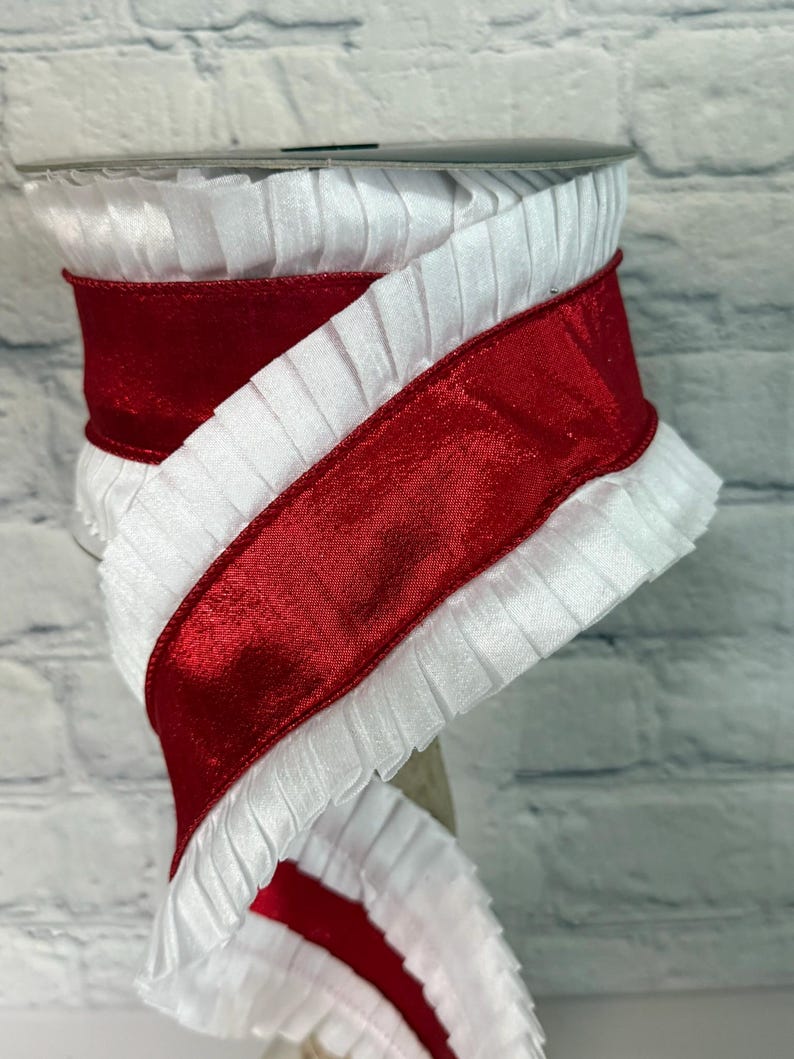 May include: A spool of white pleated ribbon with a wide, glossy red satin ribbon wrapped around it. The ribbon is likely used for crafts, gift wrapping, or decorative purposes. The white ribbon has a ruffled edge.