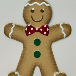 May include: A gingerbread man cookie cutout with white icing, red and white polka dot bow tie, and green buttons.