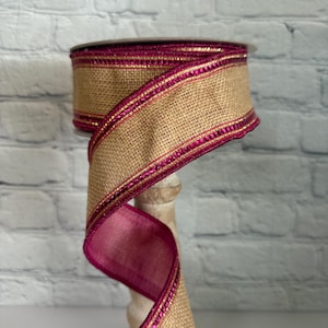 May include: A roll of burlap ribbon with a pink and gold trim. The ribbon is on a white stand.