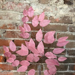 May include: A bouquet of pink artificial leaves in a clear glass vase against a brick wall background.