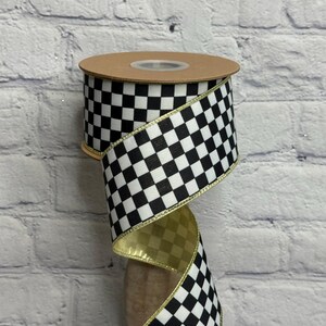 May include: A spool of ribbon featuring a black and white checkered pattern. The ribbon has a metallic gold edge on both sides and a smooth, reflective gold finish on the reverse side, wound around a circular cardboard core with a plastic center.