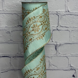 May include: A roll of decorative ribbon in a soft teal color, featuring a gold paisley design with glitter accents. The ribbon has a wired edge and is suitable for crafts, gift wrapping, and holiday decorations.