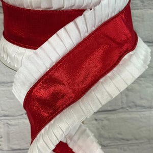 May include: A spool of decorative ribbon featuring a vibrant red satin center bordered by white ruffled edges. The ribbon is tightly wound, showcasing the contrasting textures and colors. Ideal for crafting and gift wrapping.