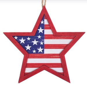 May include: A five-pointed star-shaped wall hanging featuring a red wooden frame. The center displays a printed American flag design with a distressed finish, showing white stars on a blue field on the left and horizontal red and white stripes.