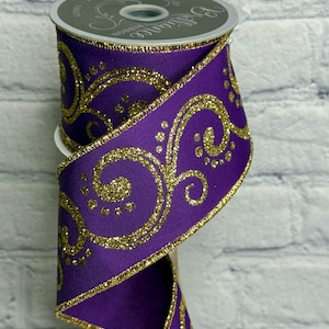 May include: A spool of purple ribbon with gold glitter scrollwork and trim. The ribbon is wrapped around a white spool. The ribbon is likely used for crafts, gift wrapping, or holiday decorations.