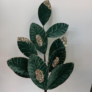 May include: A green velvet sprig with gold glitter accents. The leaves are arranged in a fan shape and have a delicate, textured appearance.