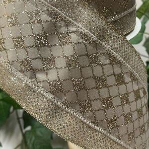 Peut inclure: Gros plan sur un ruban d&eacute;coratif avec un motif scintillant dor&eacute;. Le ruban pr&eacute;sente un motif quadrill&eacute; avec une bordure scintillante. Le ruban est de couleur beige neutre, adapt&eacute; &agrave; divers projets d'artisanat et d'emballage cadeau.