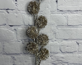 May include: A decorative floral spray featuring seven round, glitter-covered spheres arranged along a central stem. The entire piece is coated in a shimmering champagne-gold finish. A small white tag with the text Regency International is attached.