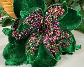 May include: A large, decorative, velvet flower in a deep emerald green. The flower's center is adorned with clusters of small, pink, gold, and green beads. The petals have a soft, textured appearance, and the overall design is elegant.