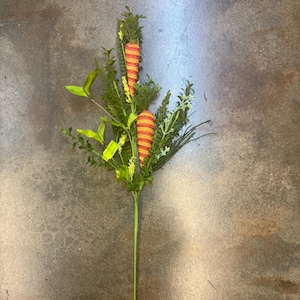 May include: A long stemmed artificial plant with green leaves and two orange and yellow striped carrots.