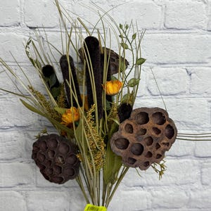 May include: A bouquet of dried flowers and grasses in a clear glass vase. The arrangement includes dark brown cattails, orange flowers, and seed pods. Green and tan grasses and foliage add texture and color to the display.