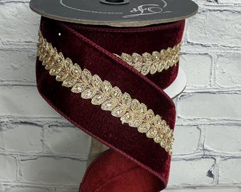 May include: A spool of deep burgundy velvet ribbon featuring a centered metallic gold embroidered leaf trim. The ribbon is wound around a black circular spool with the text Farrisilk printed in white script on the top surface of the spool.