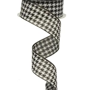 May include: A roll of black and white houndstooth patterned ribbon. The ribbon is unwound, revealing the pattern and texture. The ribbon is approximately 2.5 inches wide.