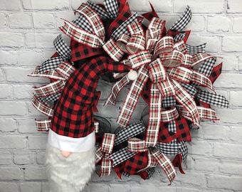 May include: A red and black buffalo plaid gnome head wreath with a white and black buffalo plaid bow. The wreath is made of mesh and has a black and white gingham ribbon.