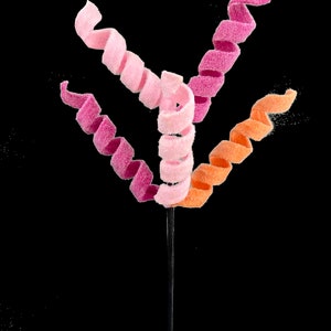 May include: Three candy swirls on a stick. The swirls are pink, light pink, and orange.