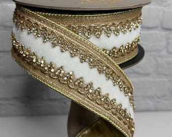 May include: A spool of white velvet ribbon with gold trim and sparkling embellishments. The ribbon has a gold metallic backing and is displayed on a wooden spool. The ribbon is ideal for crafts, gift wrapping, and holiday decorations.