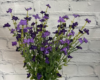 Puede incluir: Un ramo de flores artificiales moradas con tallos verdes en un jarrón de vidrio transparente. Las flores están dispuestas en un estilo suelto y natural.