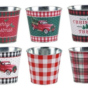 May include: Six metal Christmas themed planters with different designs. The designs include red and green plaid, red and white gingham, black and white gingham, and a red truck with a Christmas tree. The text on the planters reads "Merry Christmas" and "Farm Fresh Christmas Trees locally grown".