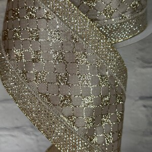 Peut inclure: Gros plan sur un ruban d&eacute;coratif &agrave; motif quadrill&eacute;. Le ruban pr&eacute;sente une base en tissu beige avec un motif quadrill&eacute; en paillettes dor&eacute;es. Les bords sont orn&eacute;s d'une bordure dor&eacute;e scintillante, cr&eacute;ant un aspect festif et &eacute;l&eacute;gant.
