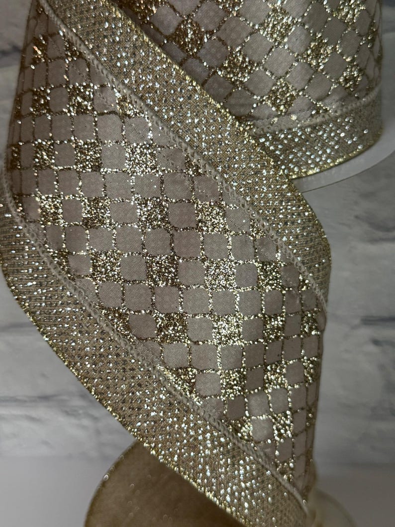 Peut inclure: Gros plan sur un ruban d&eacute;coratif &agrave; motif quadrill&eacute;. Le ruban pr&eacute;sente une base en tissu beige avec un motif quadrill&eacute; en paillettes dor&eacute;es. Les bords sont orn&eacute;s d'une bordure dor&eacute;e scintillante, cr&eacute;ant un aspect festif et &eacute;l&eacute;gant.