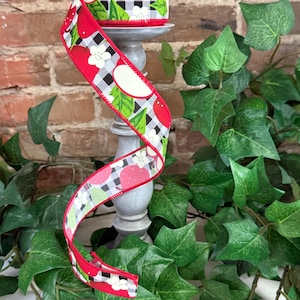 May include: Red and white ribbon with a black and white checkered pattern and a red apple design. The ribbon is wrapped around a gray candle holder.