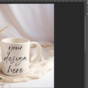 May include: White ceramic mug with a black handwritten inscription that reads "your design here" on a white fabric background with dried wheat stalks and green leaves.