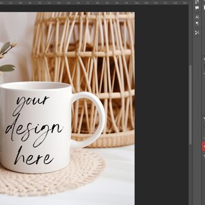 May include: White ceramic mug with a black handwritten inscription that reads "your design here" on a white surface with a beige crocheted coaster. A wicker basket is in the background.