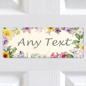 Può includere: Un cartello rettangolare per la porta con un bordo floreale. Il cartello è di colore crema con il testo "Any Text" in grigio.