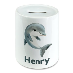 Peut inclure: Tirelire en céramique blanche avec un motif de dauphin bleu et gris. Le nom "Henry" est imprimé en noir au bas de la tirelire.