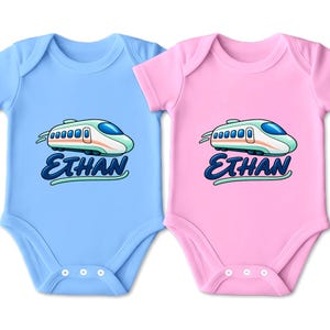 May include: Two short-sleeved baby bodysuits, one light blue and one light pink, each featuring a graphic of a stylized white and teal high-speed train above the name Ethan written in a bold, dark blue cursive font with a light teal underline.